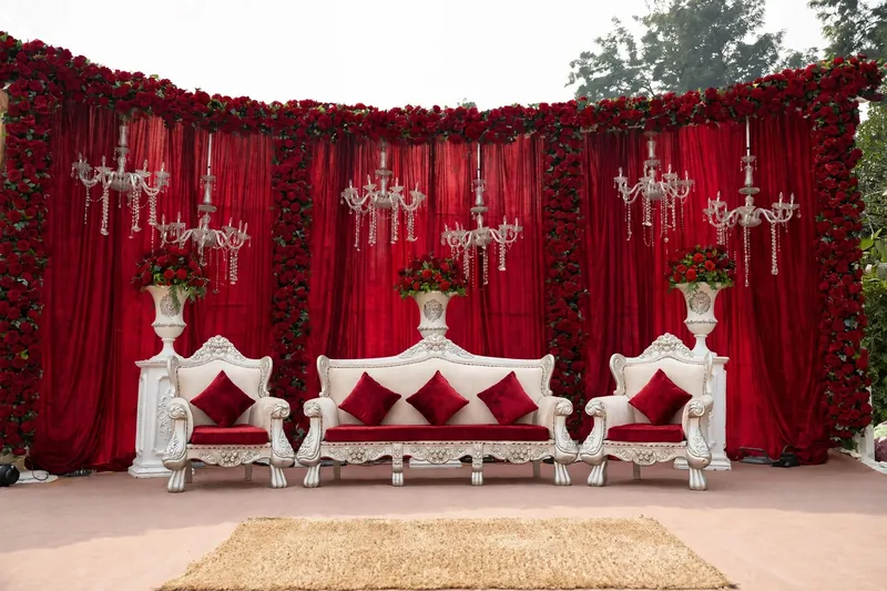 Red Drape Barat Stage with Rose Border: Red velvet drapes edged with red roses, red rose pots on white stands and hanging chandeliers, GuleGul Flowers Lahore