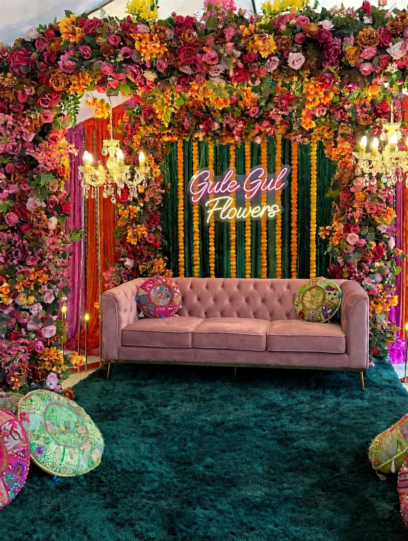 Mehndi Flower Frame with Pink Sofa: Frame of roses and marigolds around a green backdrop with genda strings, a pink sofa and floor cushions, GuleGul Flowers Lahore